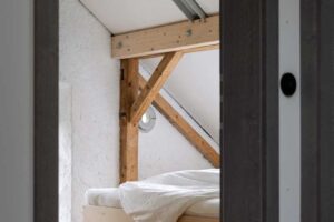 Pohled do ložnice s vestavěnou postelí dřevěnou podlahou a přiznaným krovem