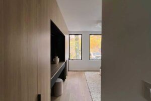 Pohled ze vstupu do ložnice s vestavěnými dubovými skříněmi a klidným výhledem do zeleně za okny.