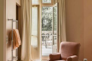 Vstup na terasu se světlými závěsy, křeslem a výhledem do zámeckého parku