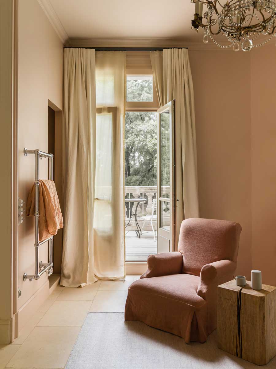 Vstup na terasu se světlými závěsy, křeslem a výhledem do zámeckého parku