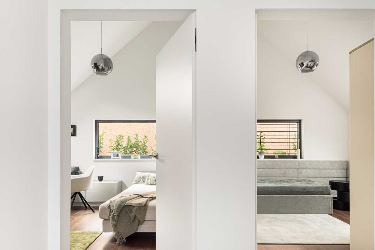 Průhled mezi dvěma místnostmi s bílými stěnami, sedacím nábytkem a pracovním koutem v pozadí.