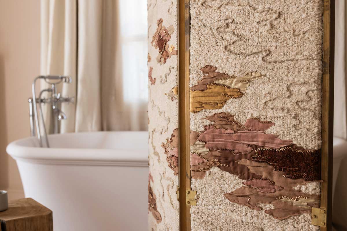 Detail textilní zástěny v koupelně s ruční výšivkou a jemnou strukturou látky