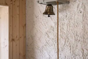 Detail zvonku s provazem na hrubé omítce v interiéru chalupy