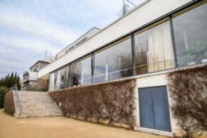 Uliční pohled na Vilou Tugendhat s jednoduchou bílou fasádou a pásovými okny.