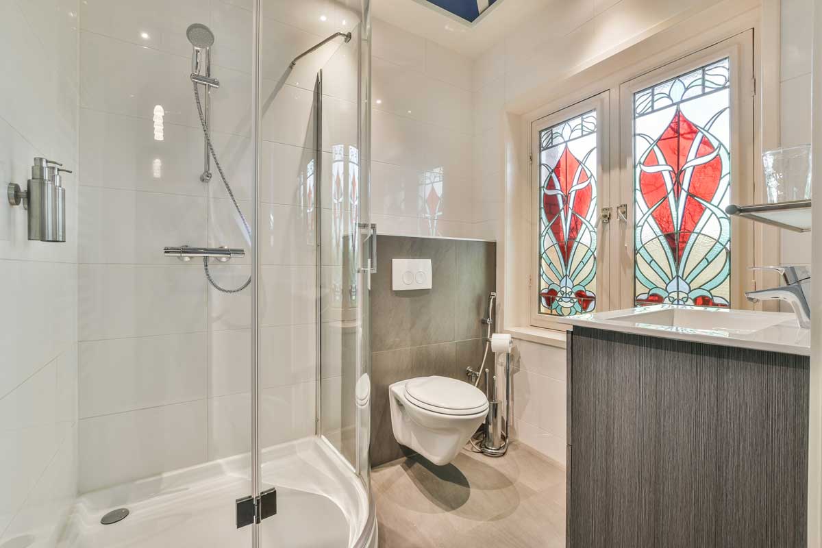 Dekorativní barevné sklo v koupelně filtruje světlo a propojuje intimitu prostoru s výtvarným akcentem inspirovaným tradicí.