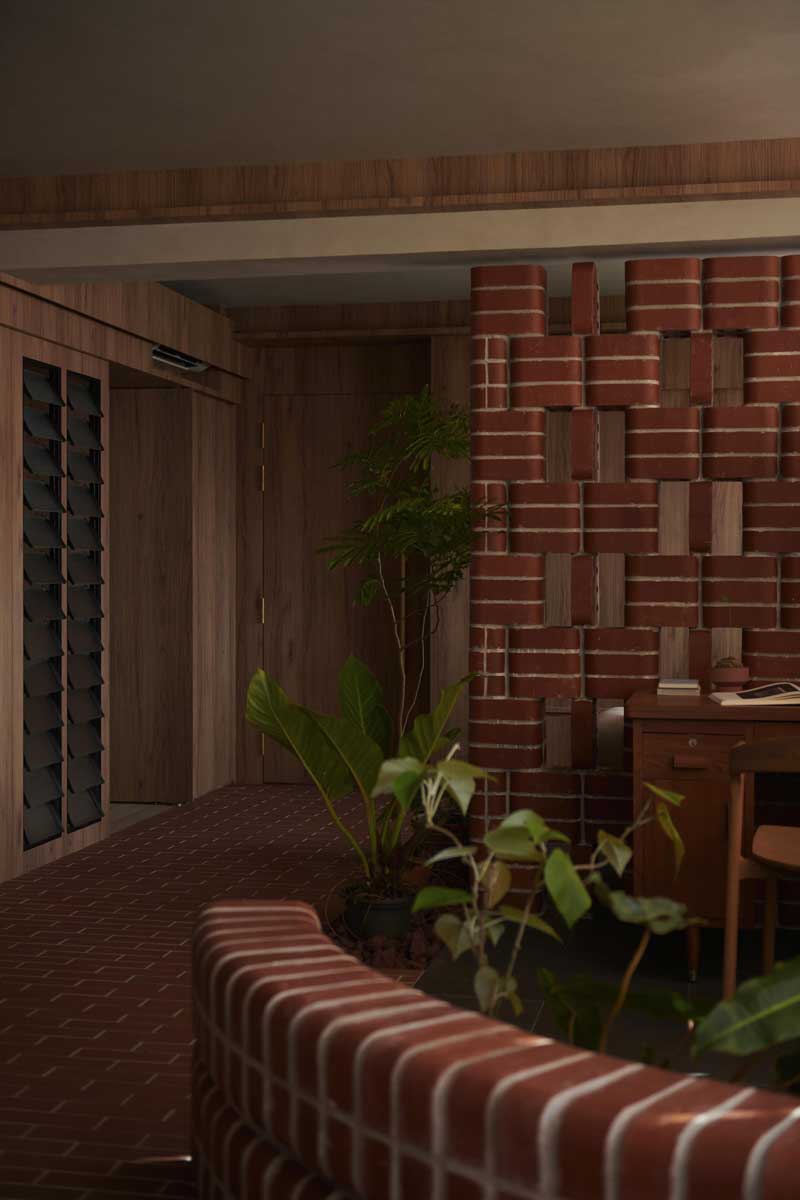 Zakřivená cihlová stěna jemně odděluje pracovní kout od vstupní části bytu a vytváří pocit malého parku uvnitř interiéru.