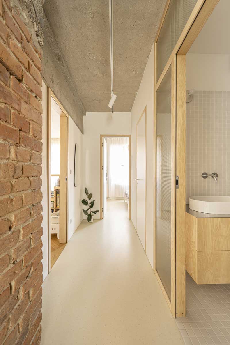 Světlá chodba s přiznanou cihlovou stěnou a prosklenými dveřmi po rekonstrukci bytu
