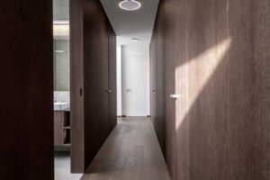 Interiér chodby s tmavým dřevěným obkladem, minimalistickými dveřmi a dřevěnou podlahou.