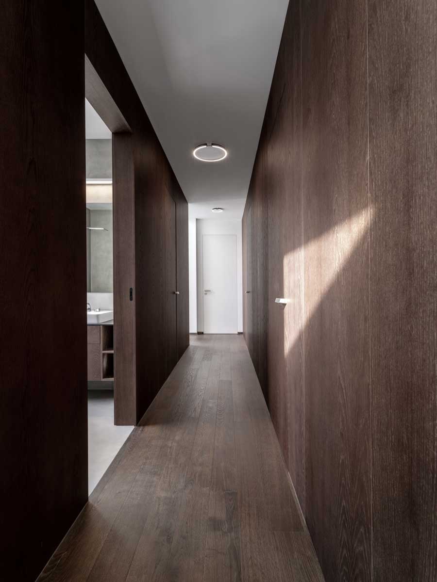 Interiér chodby s tmavým dřevěným obkladem, minimalistickými dveřmi a dřevěnou podlahou.