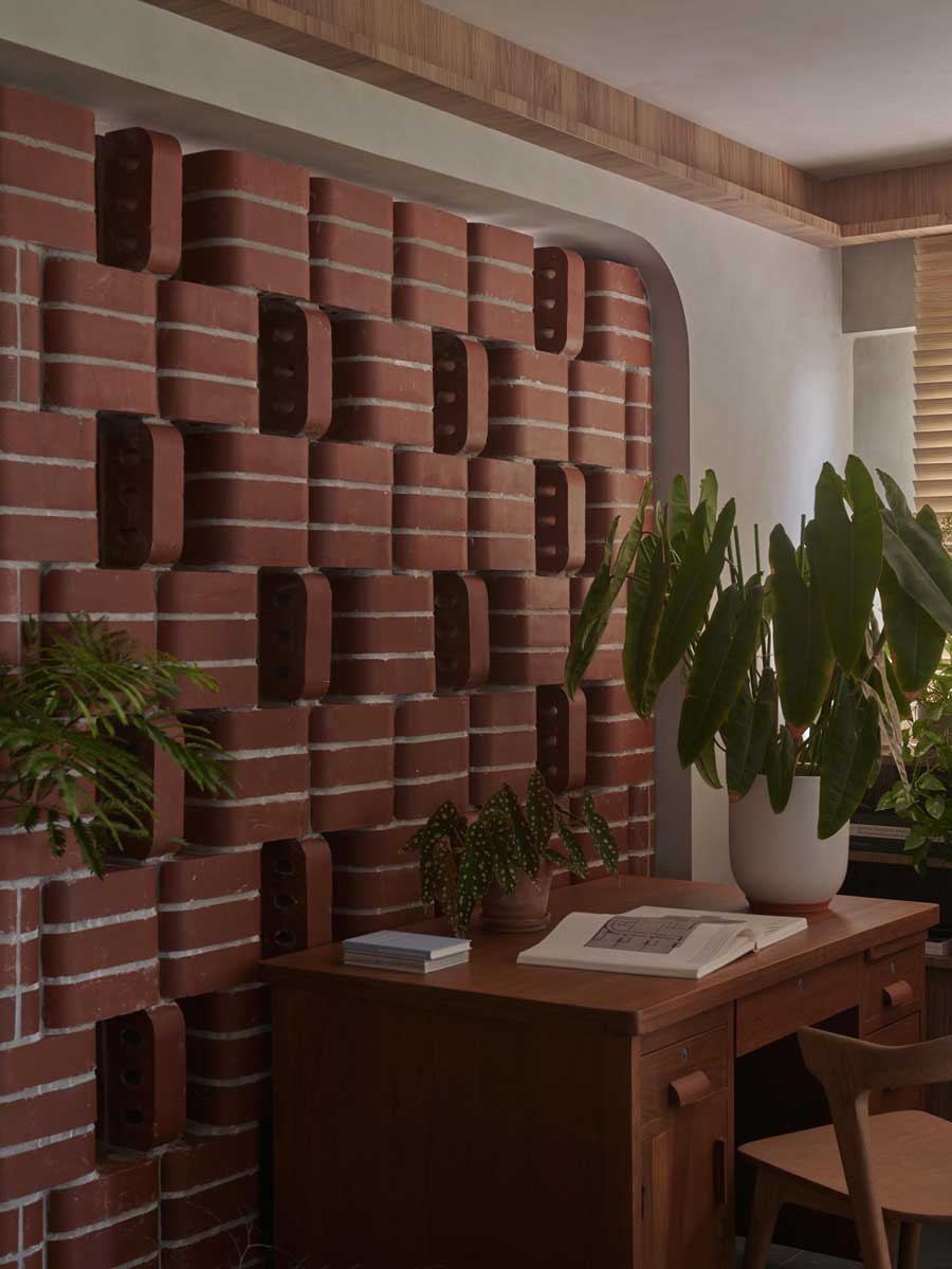 Volně stojící stěna z obloukových cihel jemně odděluje pracovní kout a zároveň umožňuje průhled do zelené části bytu.