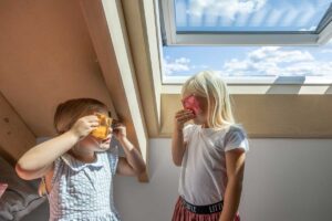 Děti v podkrovním pokoji nízkoenergetické dřevostavby osvětleném velkým střešním oknem