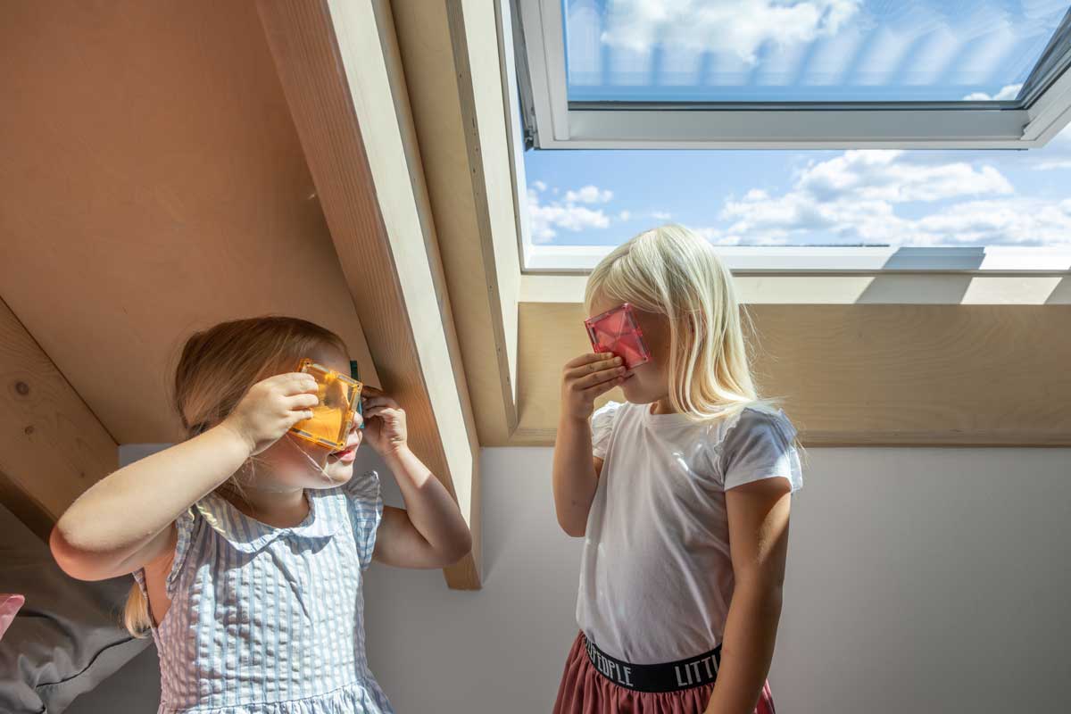 Děti v podkrovním pokoji nízkoenergetické dřevostavby osvětleném velkým střešním oknem