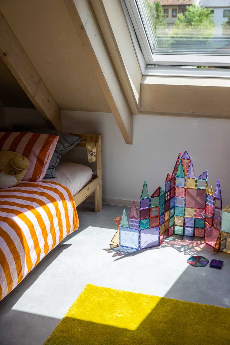 Dětský pokoj v udržitelné dřevostavbě s velkým střešním oknem a přiznanou dřevěnou konstrukcí