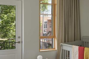 Světlý dětský pokoj s velkým oknem, přírodními materiály a jednoduchým vybavením.