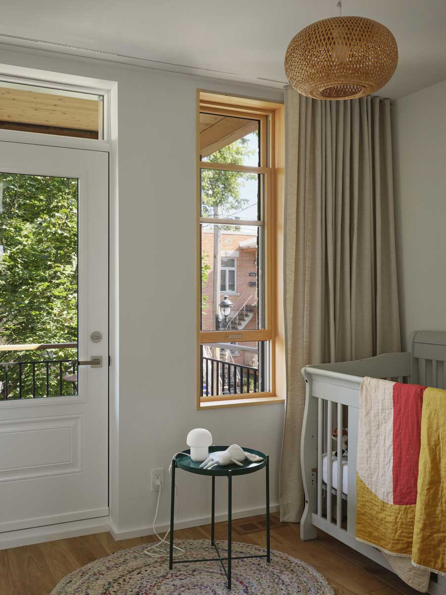 Světlý dětský pokoj s velkým oknem, přírodními materiály a jednoduchým vybavením.