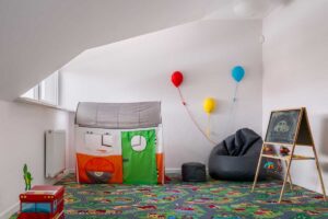 Podkrovní dětský kout s hracím kobercem, stanem a kreativní tabulí vytváří bezpečné a hravé prostředí pod šikminou.