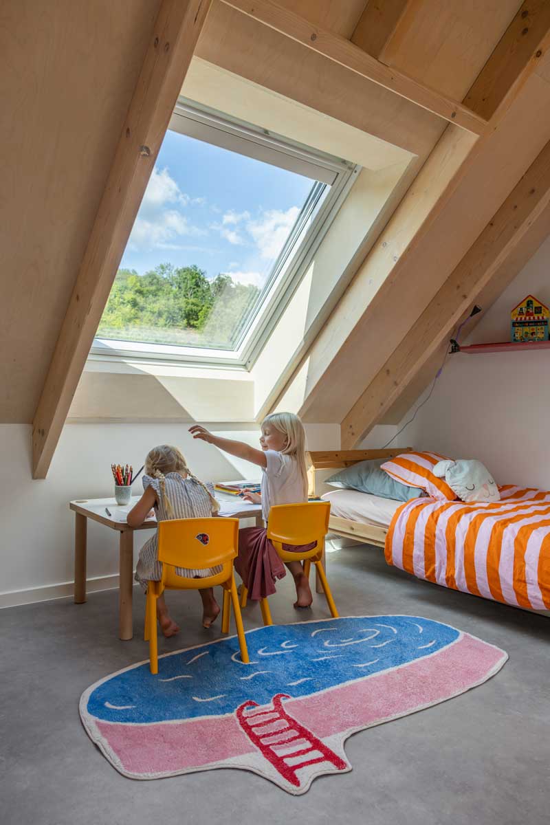 Dětský pracovní kout pod střešním oknem v nízkoenergetické dřevostavbě s důrazem na denní světlo a přirozené větrání