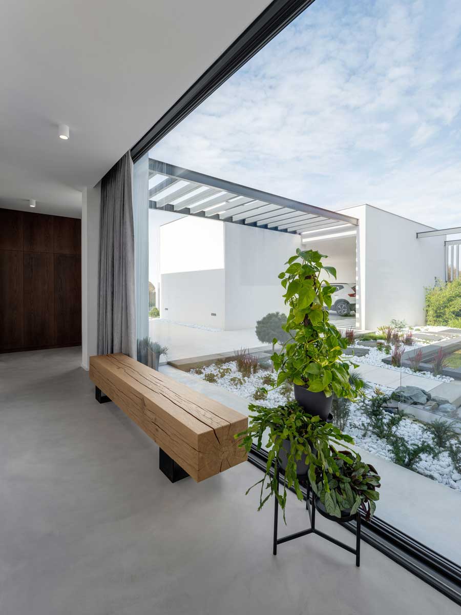 Masivní dřevěná lavice u velkoformátového okna s výhledem do zahrady.