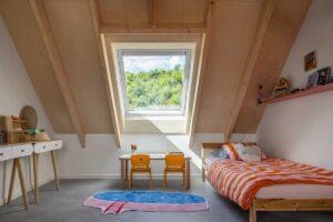 Dětský pokoj v podkroví dřevostavby se střešním oknem VELUX a dřevěnými trámy v interiéru