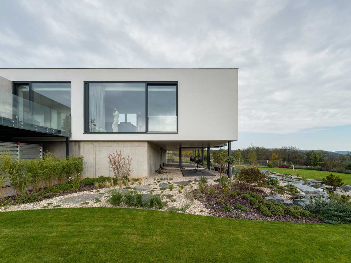 Moderní rodinný dům s velkým prosklením a přírodní zahradou s trvalkami a kameny.