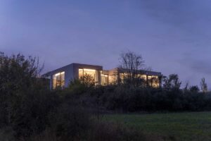 Moderní kubický dům na vyvýšeném pozemku při soumraku.