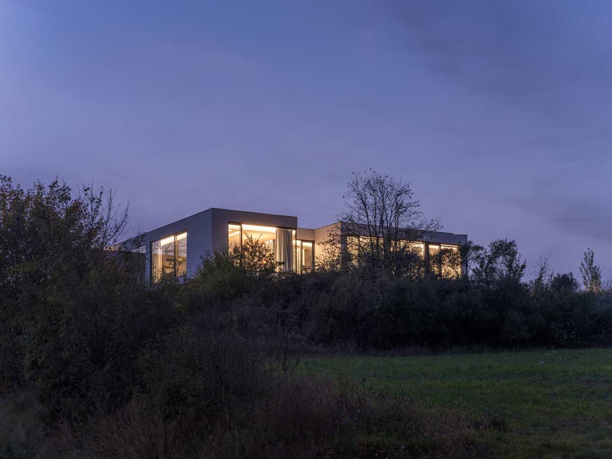 Moderní kubický dům na vyvýšeném pozemku při soumraku.