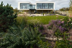 Pohled na moderní dům s velkými okny a upraveným trávníkem v popředí.