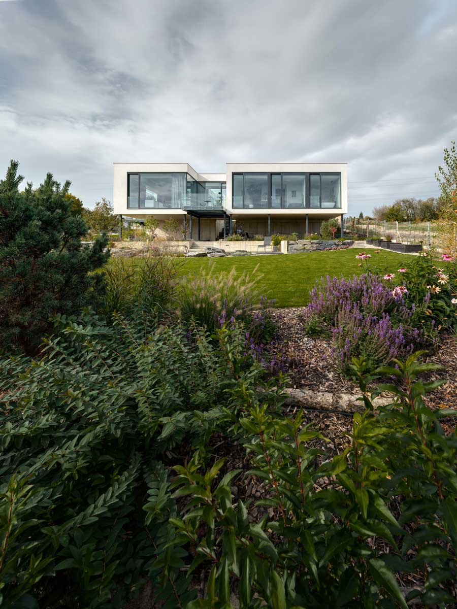 Pohled na moderní dům s velkými okny a upraveným trávníkem v popředí.