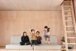 Rodina sedí na jednoduché vestavěné pohovce v dřevěném interiéru s mezonetem nad hlavou.