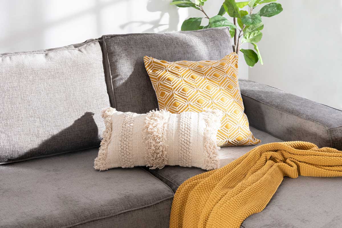 Šedá pohovka s hustě tkanými polštáři a dekorativními textiliemi.