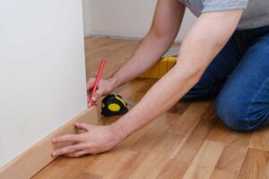 Montáž soklové lišty podél stěny při dokončování podlahy, která zakrývá dilatační spáru a nerovnosti.