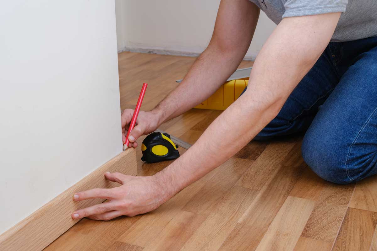 Montáž soklové lišty podél stěny při dokončování podlahy, která zakrývá dilatační spáru a nerovnosti.