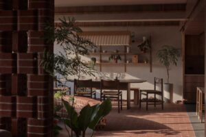 Jídelna obklopená pokojovými rostlinami a zakřivenou cihlovou lavicí působí jako klidné místo uprostřed domácího parku.