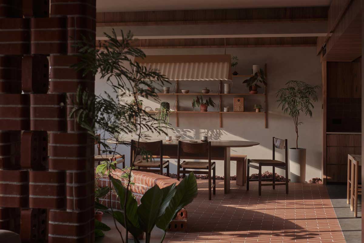 Jídelna obklopená pokojovými rostlinami a zakřivenou cihlovou lavicí působí jako klidné místo uprostřed domácího parku.