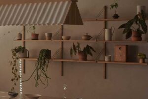 Oválný jídelní stůl z tmavého dřeva je obklopen jednoduchými židlemi a otevřenými policemi s rostlinami a keramikou.