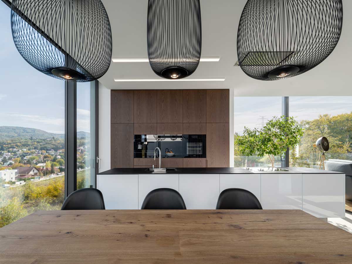 Jídelní kout s masivním dřevěným stolem, černými designovými židlemi a panoramatickým oknem.