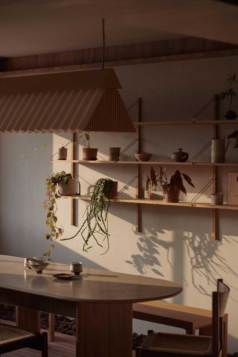 Jídelní kout propojuje dřevěný nábytek, otevřené police a bohatou zeleň, která je přirozenou součástí každodenního života.