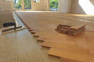 Lepení dřevěné parketové podlahy na připravený podklad pomocí zubové stěrky, s důrazem na přesné napojení jednotlivých dílců.