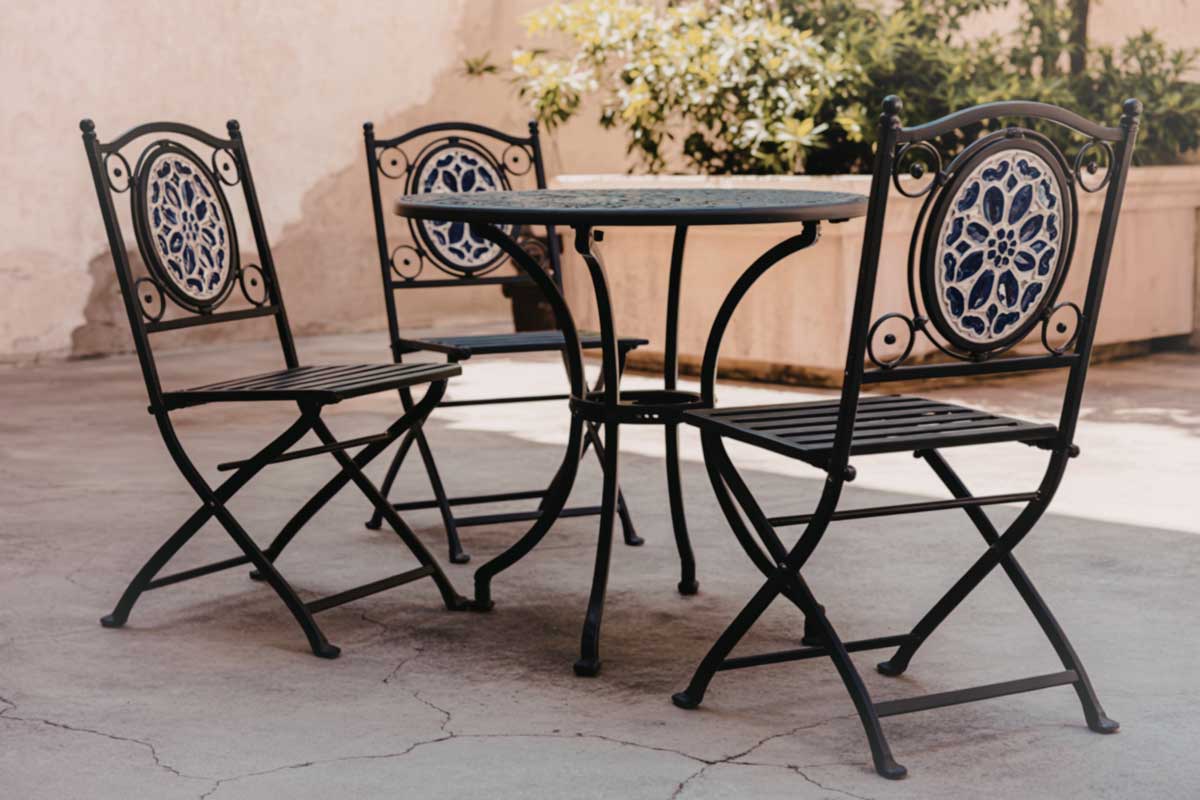 Kovový zahradní stolek a skládací židle s dekorativními opěradly.