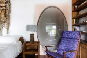 Křeslo v ložnici doplněné výrazným uměleckým prvkem vytváří osobní kout pro odpočinek i tvůrčí myšlení.