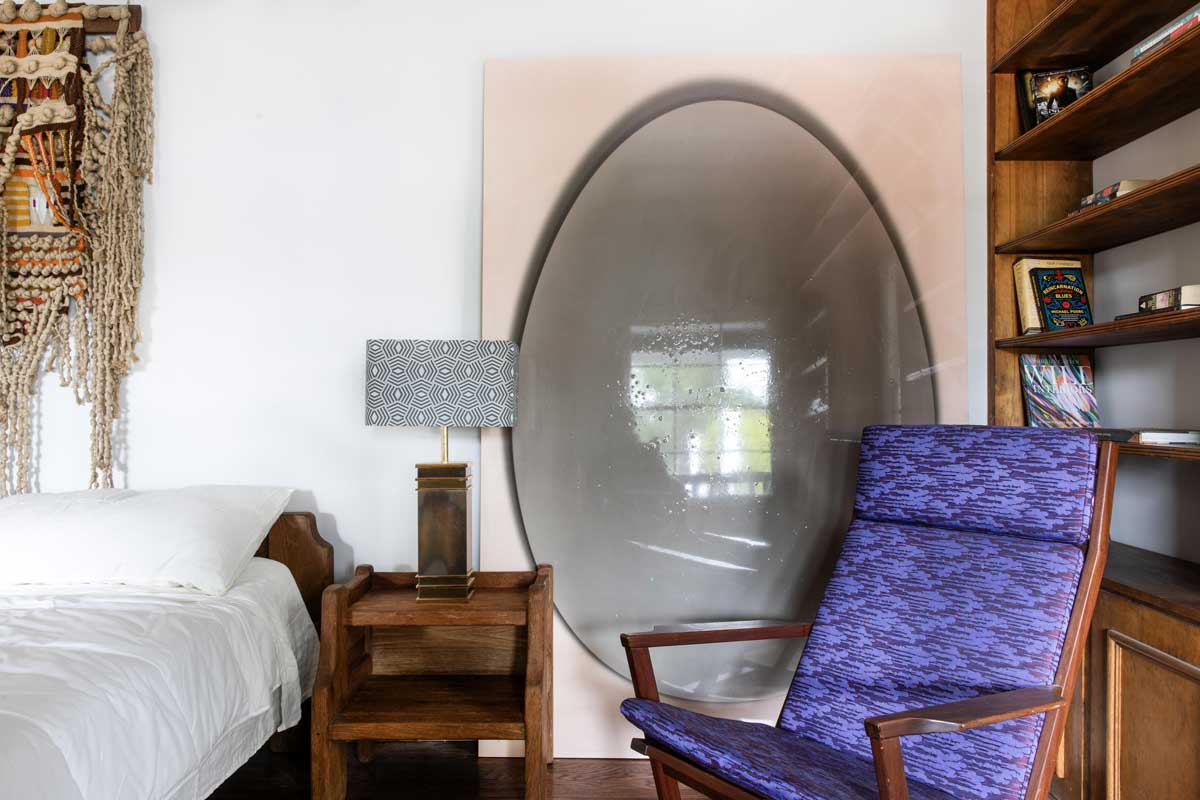 Křeslo v ložnici doplněné výrazným uměleckým prvkem vytváří osobní kout pro odpočinek i tvůrčí myšlení.