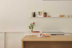 Jednoduchá bílá kuchyň s otevřenou policí, integrovanou digestoří ve stropě a světlým obkladem.