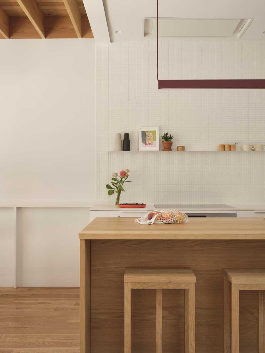 Jednoduchá bílá kuchyň s otevřenou policí, integrovanou digestoří ve stropě a světlým obkladem.