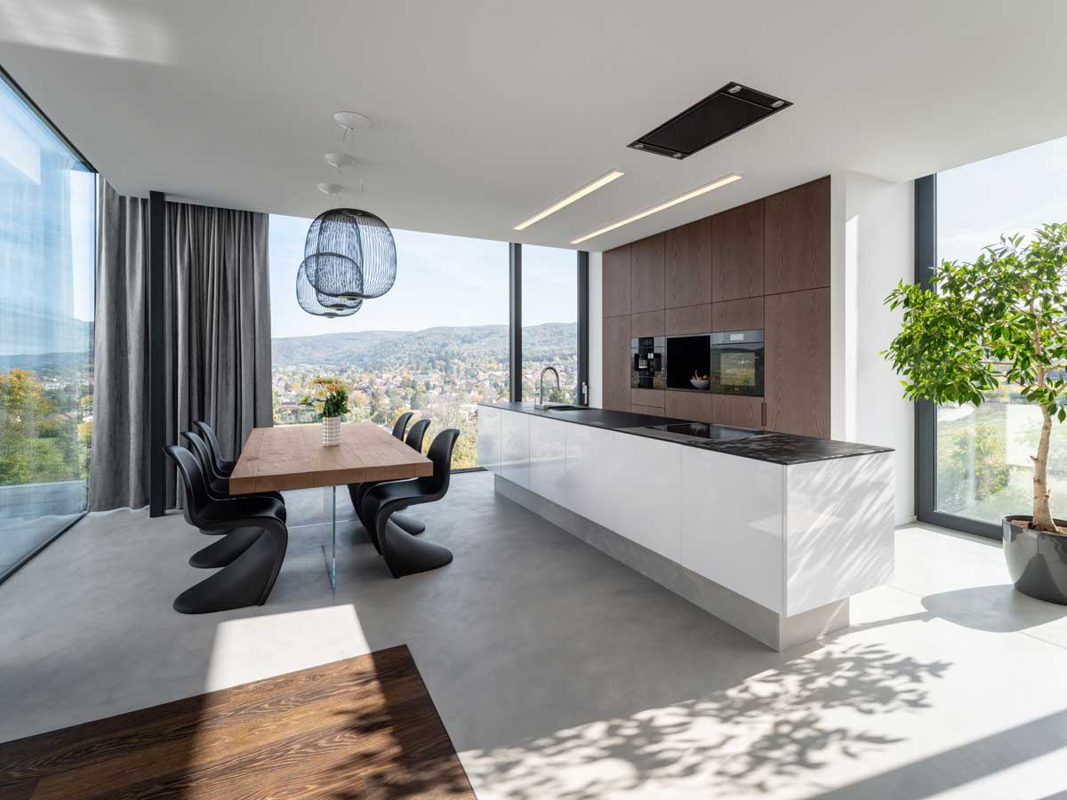 Otevřený obytný prostor s kuchyní a jídelnou, velkoformátová okna a minimalistický nábytek.