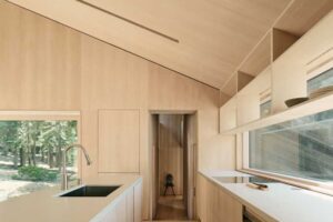 Úzká kuchyně s vestavěným nábytkem ze světlého dřeva a velkým oknem propojuje interiér s okolním lesem.