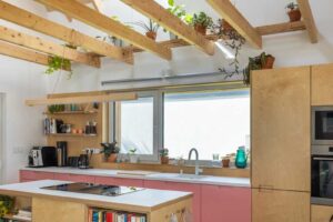 Moderní kuchyně v nízkoenergetické dřevostavbě s růžovými spodními skříňkami a přiznanými dřevěnými trámy