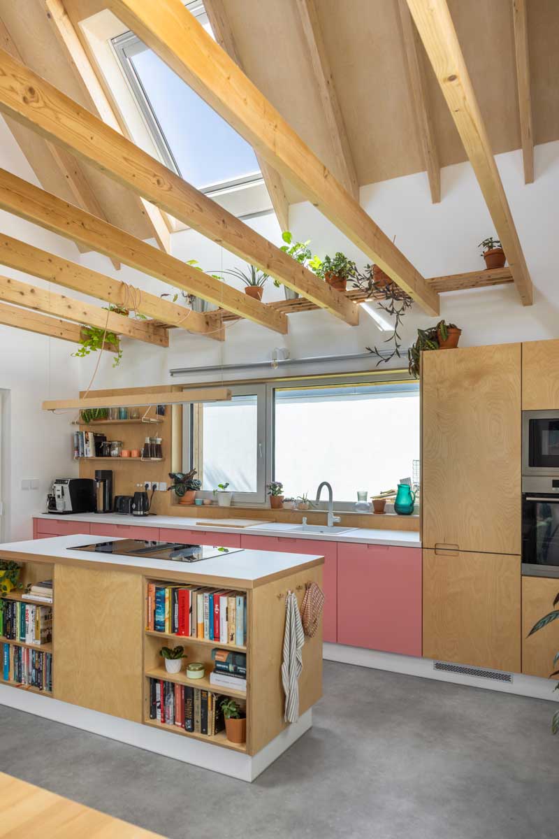 Moderní kuchyně v nízkoenergetické dřevostavbě s růžovými spodními skříňkami a přiznanými dřevěnými trámy