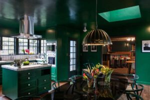 Tmavě zelená kuchyně s výraznými svítidly a kontrastními detaily funguje jako aktivní centrum domu.