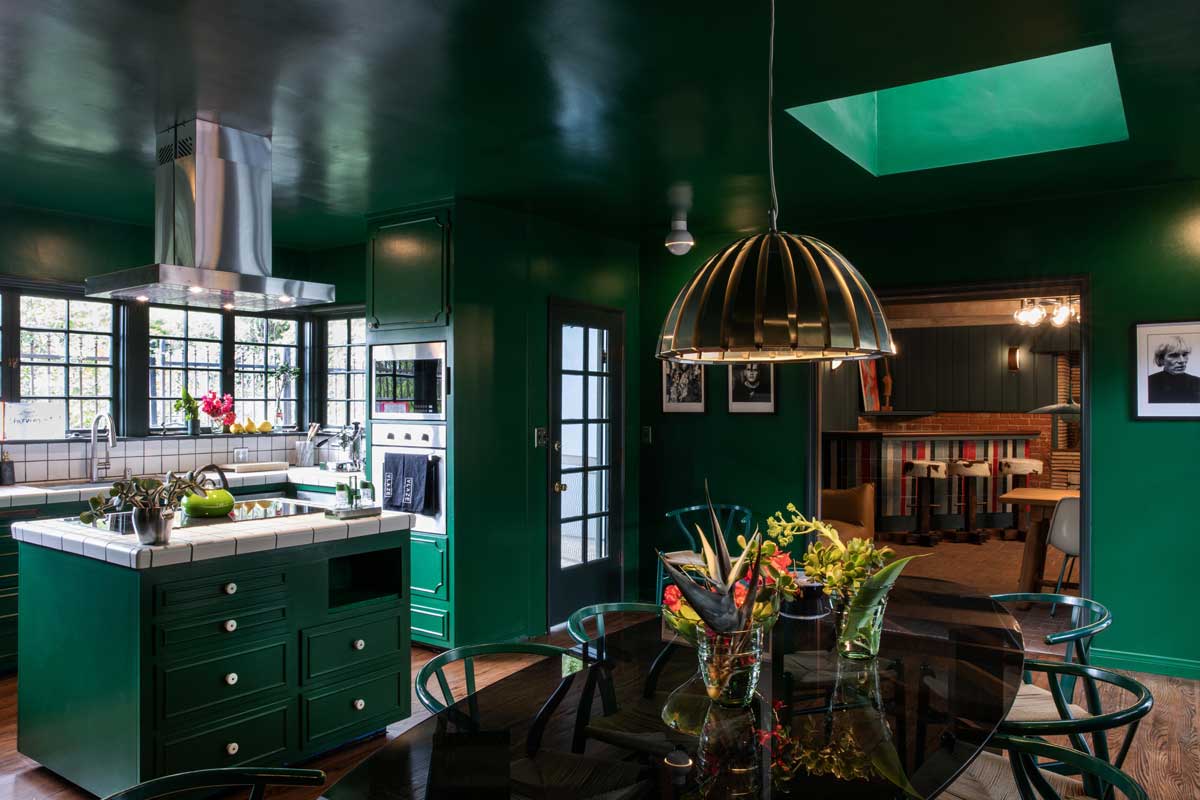Tmavě zelená kuchyně s výraznými svítidly a kontrastními detaily funguje jako aktivní centrum domu.