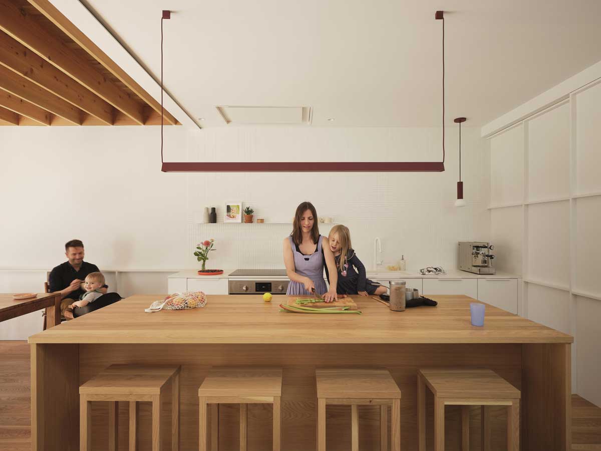 Rodina u velkého kuchyňského ostrůvku z masivního dřeva v otevřeném přízemí domu.